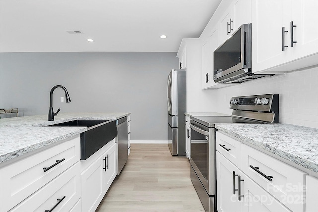 kitchen with a sink, visible vents, appliances with stainless steel finishes, decorative backsplash, and light wood finished floors