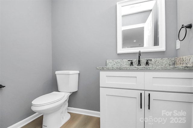 half bath with vanity, wood finished floors, toilet, and baseboards