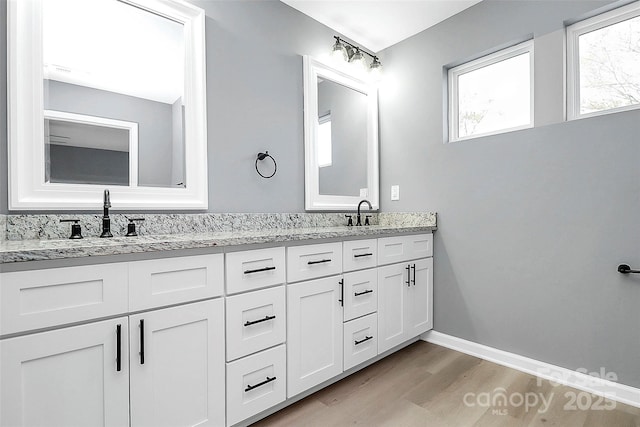 full bath featuring double vanity, a sink, baseboards, and wood finished floors