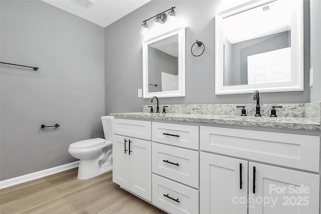 bathroom with double vanity, toilet, a sink, wood finished floors, and baseboards