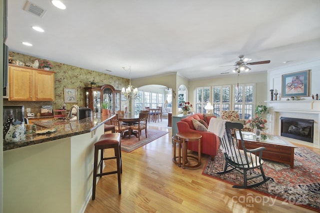 kitchen with open floor plan, dark stone countertops, light wood-type flooring, a kitchen bar, and a fireplace