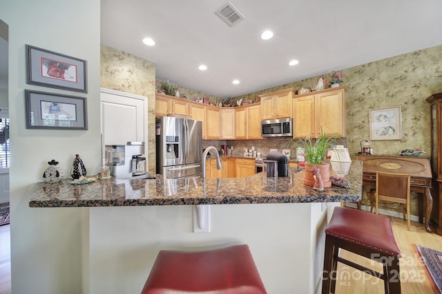 kitchen featuring stainless steel appliances, visible vents, a peninsula, a kitchen breakfast bar, and wallpapered walls