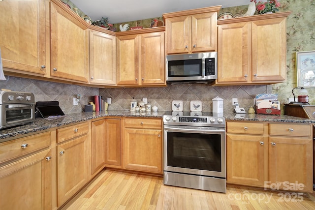 kitchen featuring light wood-style floors, tasteful backsplash, stainless steel appliances, and dark stone countertops