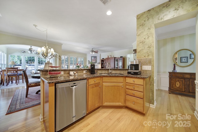 kitchen with stainless steel dishwasher, ornamental molding, a sink, dark stone countertops, and wallpapered walls