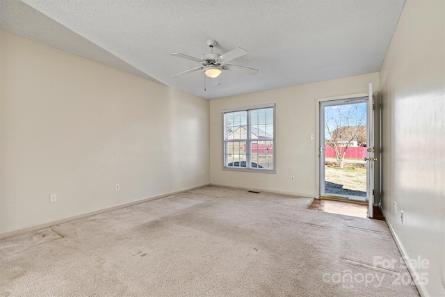 carpeted spare room with a textured ceiling, visible vents, a ceiling fan, and baseboards