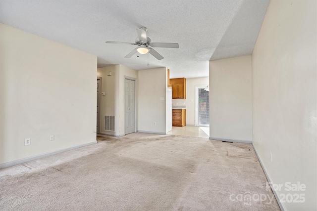 empty room with a textured ceiling, light carpet, visible vents, baseboards, and a ceiling fan