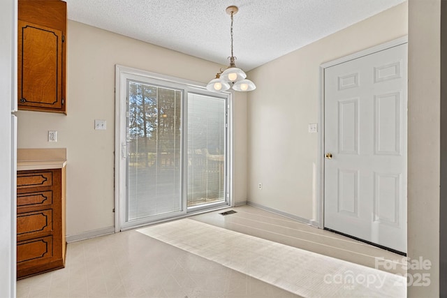 unfurnished dining area featuring light floors, a notable chandelier, a textured ceiling, and baseboards