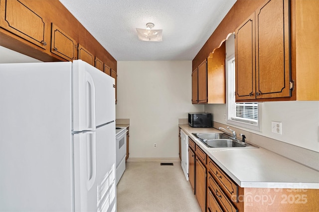 kitchen with white appliances, brown cabinetry, light countertops, a textured ceiling, and a sink