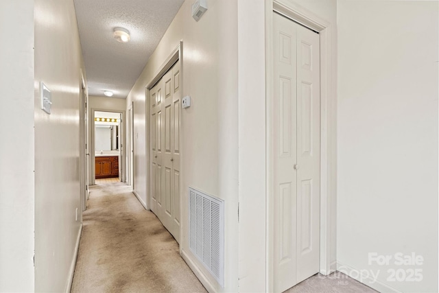 corridor with light carpet, baseboards, visible vents, and a textured ceiling