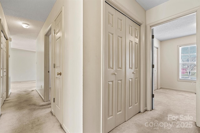 hall featuring light colored carpet, a textured ceiling, and baseboards