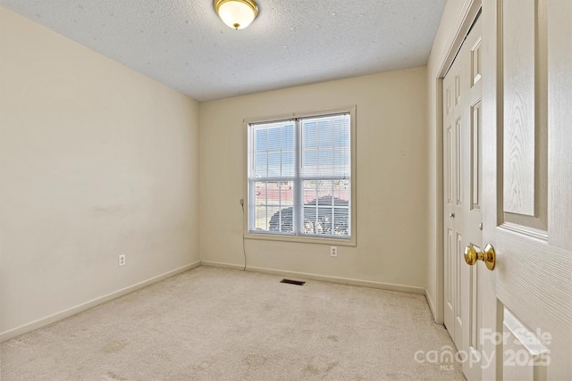 unfurnished bedroom with a closet, visible vents, carpet flooring, a textured ceiling, and baseboards