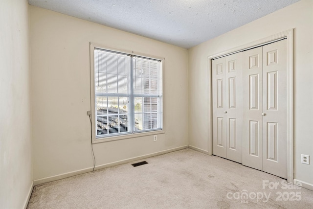 unfurnished bedroom featuring a textured ceiling, visible vents, baseboards, a closet, and carpet