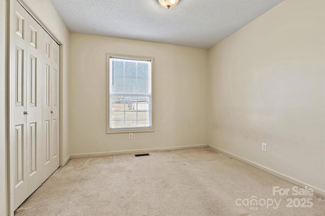 unfurnished bedroom featuring a textured ceiling, carpet floors, visible vents, baseboards, and a closet