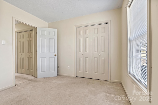 unfurnished bedroom with a closet, light colored carpet, a textured ceiling, and baseboards