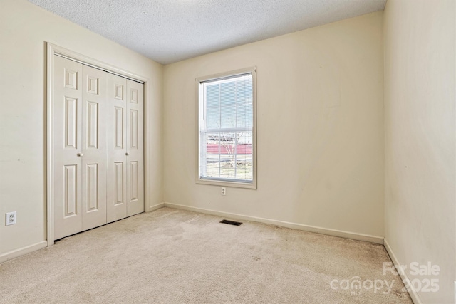 unfurnished bedroom with baseboards, visible vents, carpet, a textured ceiling, and a closet