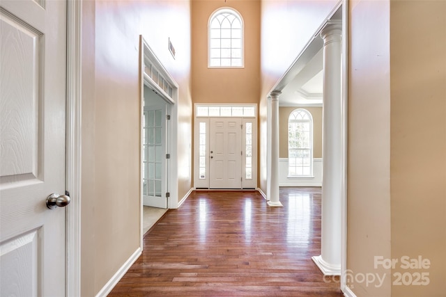 foyer entrance with decorative columns, a high ceiling, baseboards, and wood finished floors