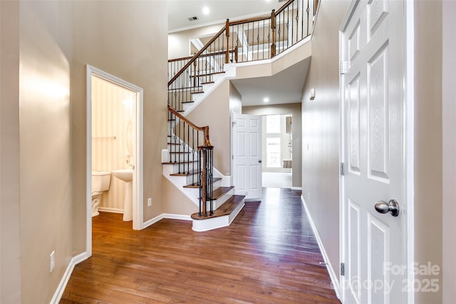 entrance foyer with wood finished floors, visible vents, a towering ceiling, stairs, and baseboards