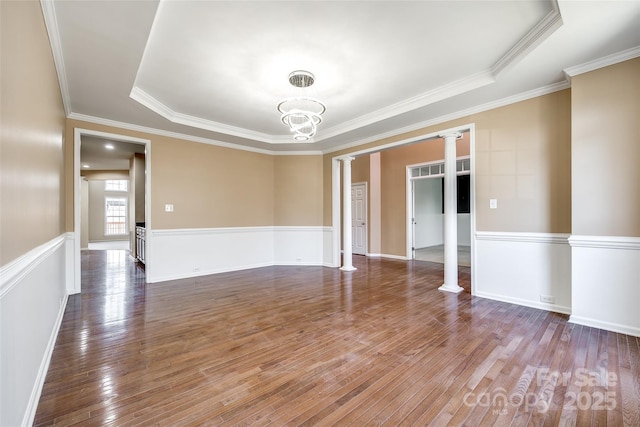 unfurnished room with hardwood / wood-style floors, ornamental molding, ornate columns, a tray ceiling, and an inviting chandelier