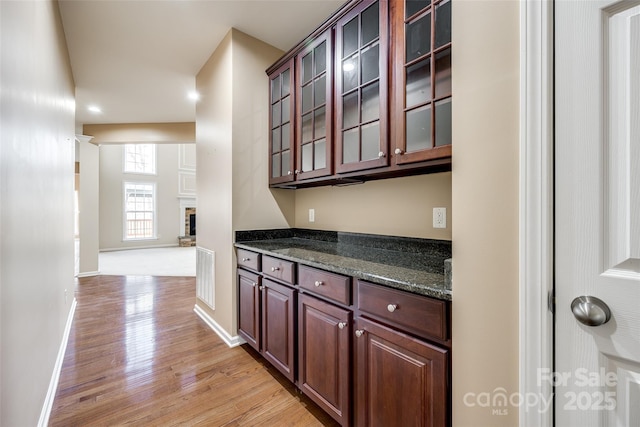 kitchen with visible vents, light wood-style floors, glass insert cabinets, dark stone counters, and baseboards