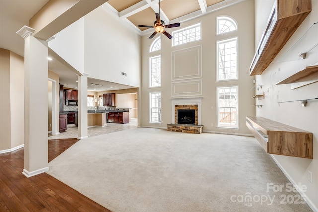 unfurnished living room featuring ornate columns, coffered ceiling, carpet flooring, and a stone fireplace