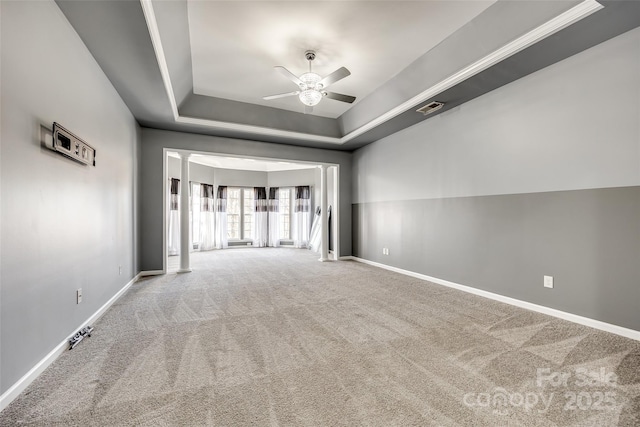 carpeted empty room with ceiling fan, a raised ceiling, visible vents, and baseboards