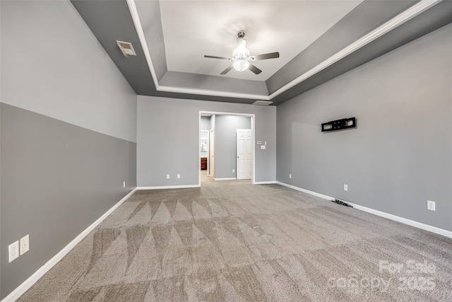 empty room with carpet floors, a raised ceiling, and baseboards