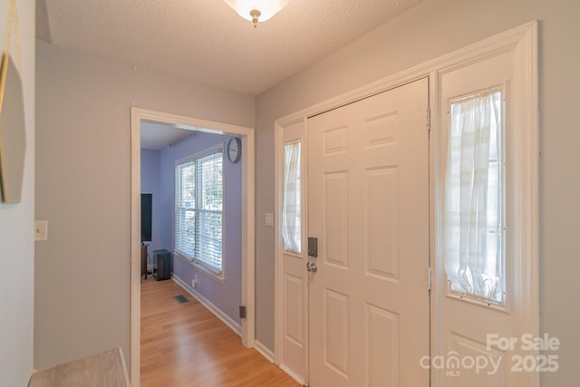 foyer featuring a textured ceiling, baseboards, visible vents, and light wood-style floors