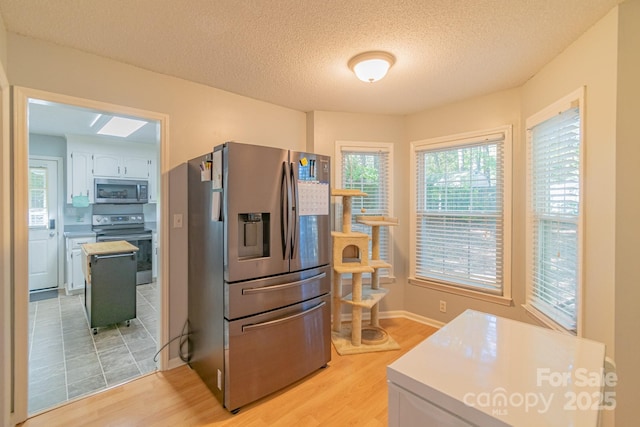 kitchen featuring light wood-type flooring, appliances with stainless steel finishes, light countertops, and a textured ceiling