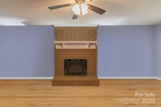 unfurnished living room featuring a brick fireplace, a textured ceiling, baseboards, and wood finished floors