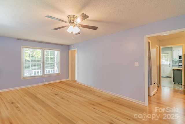 empty room with a textured ceiling, ceiling fan, light wood-style flooring, and baseboards