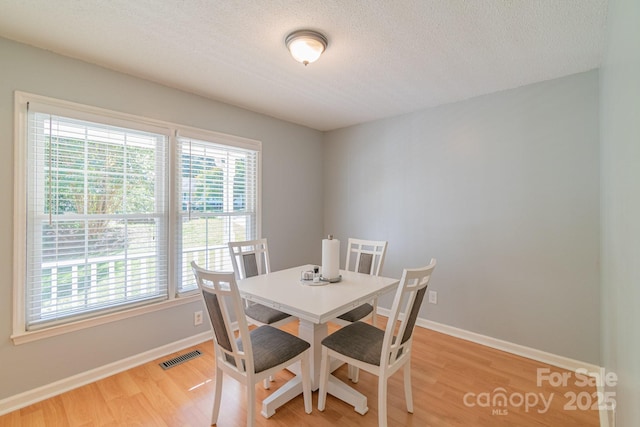 dining room featuring baseboards, a textured ceiling, visible vents, and light wood-style floors