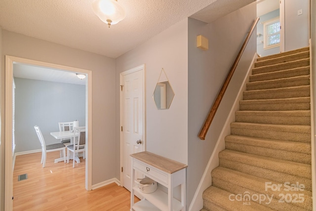 stairway with visible vents, a textured ceiling, baseboards, and wood finished floors