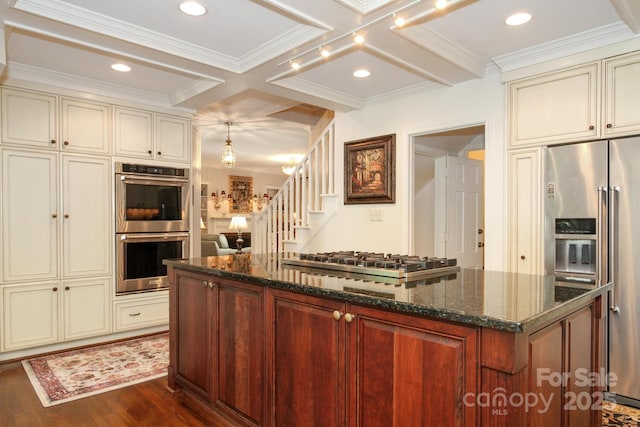 kitchen featuring dark stone counters, appliances with stainless steel finishes, cream cabinetry, coffered ceiling, and dark wood-style flooring