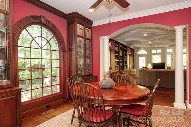 dining space with ornamental molding, a ceiling fan, wood finished floors, arched walkways, and decorative columns