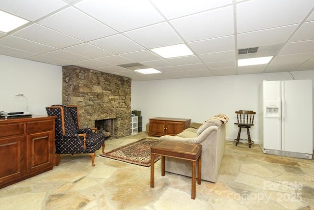 living area with a stone fireplace, stone finish floor, a paneled ceiling, and visible vents