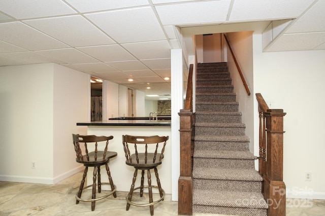 stairs with a drop ceiling, baseboards, and indoor bar