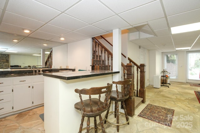 kitchen featuring a breakfast bar, dark countertops, white cabinets, and a paneled ceiling