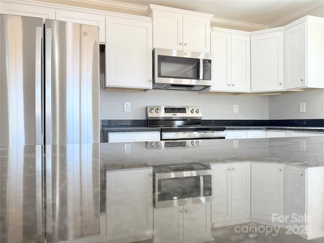 kitchen featuring dark stone counters, appliances with stainless steel finishes, ornamental molding, and white cabinetry