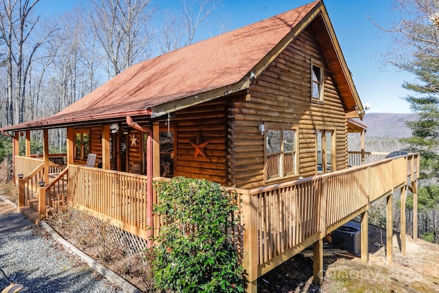 view of side of home featuring roof with shingles, a mountain view, and log siding