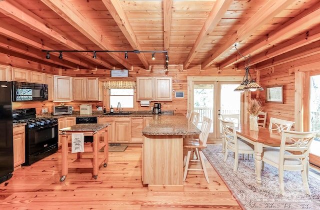 kitchen with light brown cabinetry, a peninsula, wood walls, black appliances, and a sink