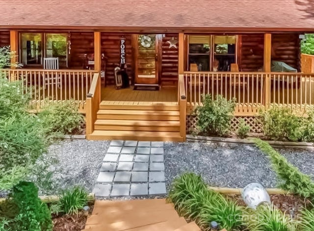 doorway to property featuring a porch, log exterior, and roof with shingles