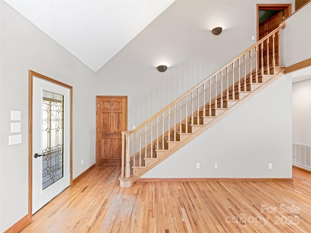 foyer entrance with visible vents, vaulted ceiling, baseboards, and wood finished floors