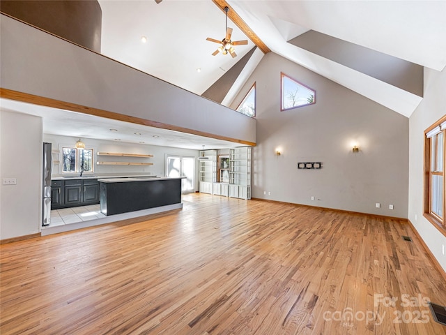 unfurnished living room featuring light wood finished floors, a ceiling fan, a sink, high vaulted ceiling, and baseboards