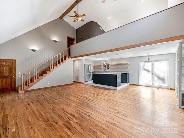 unfurnished living room with high vaulted ceiling, a ceiling fan, stairs, light wood finished floors, and beamed ceiling