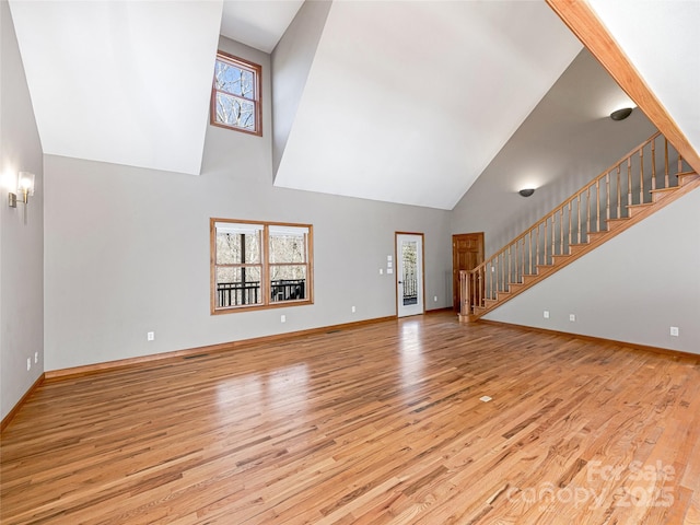 unfurnished living room featuring high vaulted ceiling, light wood-style flooring, baseboards, and stairs