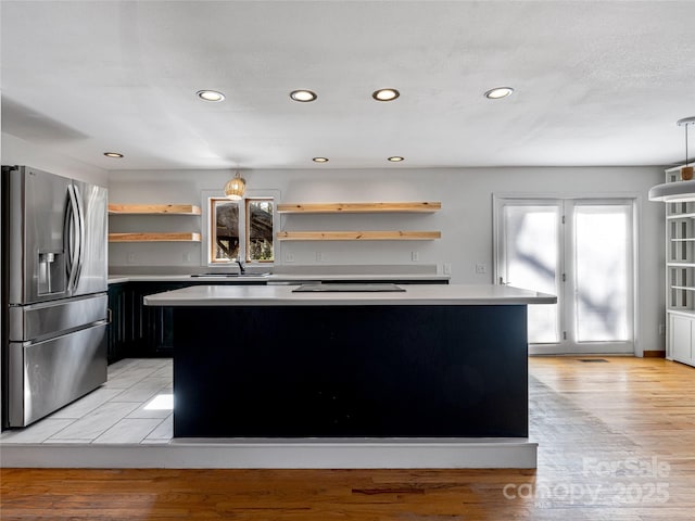 kitchen with open shelves, light countertops, a center island, and stainless steel fridge with ice dispenser