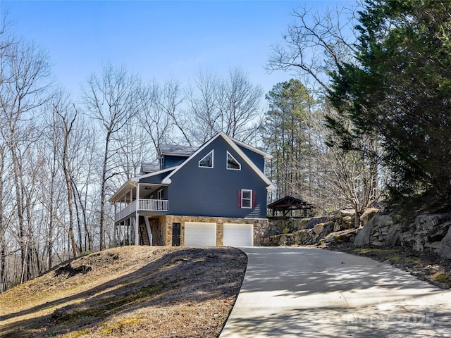 view of front of house with a porch, a garage, stone siding, driveway, and stairs