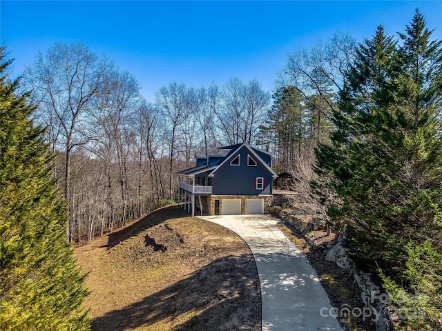 traditional home featuring an attached garage, stone siding, driveway, and a forest view