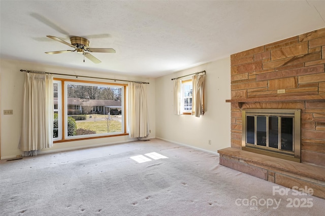 unfurnished living room featuring carpet, a ceiling fan, a stone fireplace, a textured ceiling, and baseboards