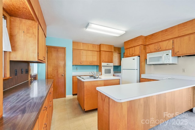 kitchen featuring light countertops, a kitchen island with sink, a sink, white appliances, and a peninsula